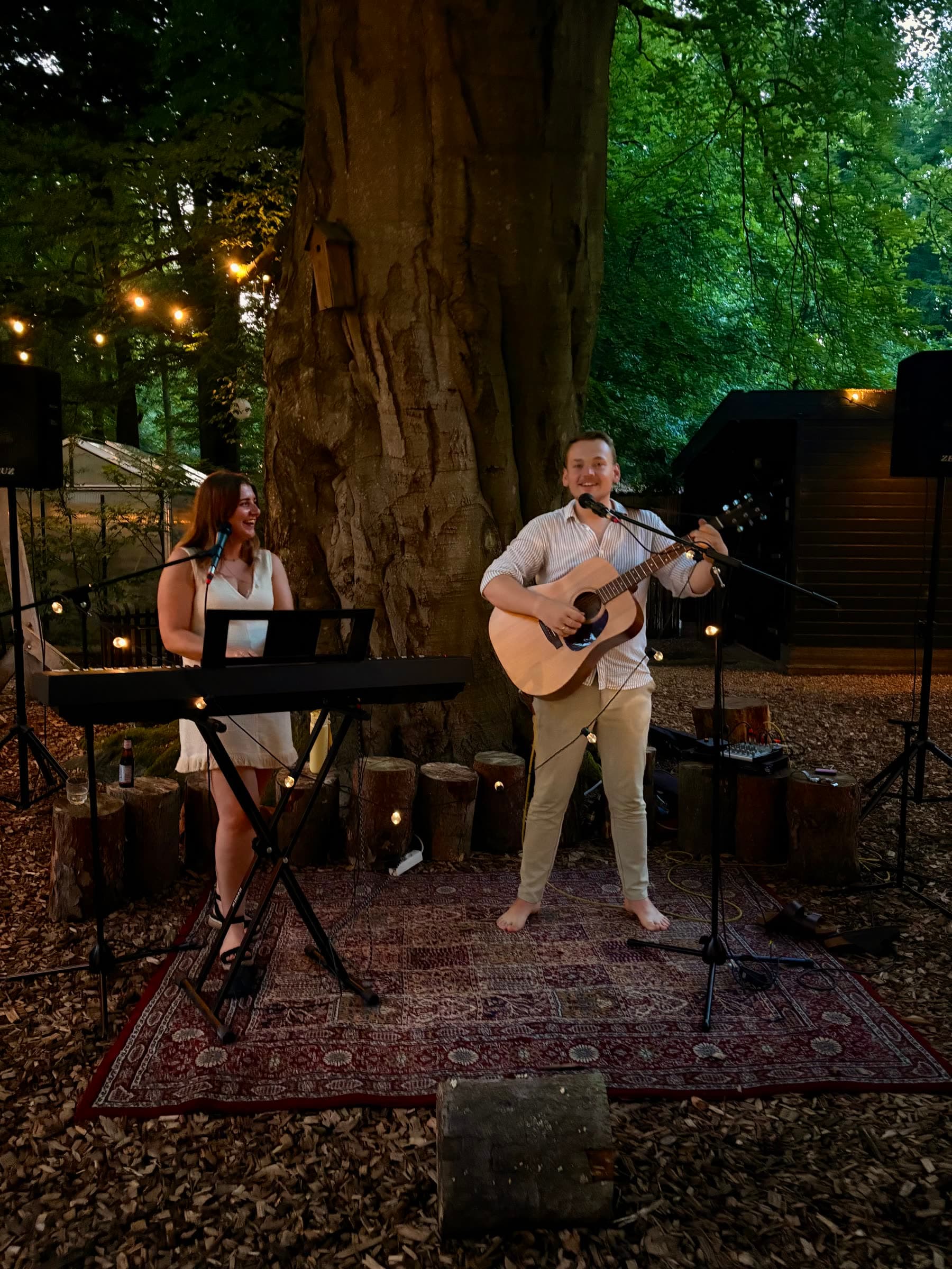 Laura zingt met gastgitarist op een avondbruiloft in het bos onder lichtsnoeren